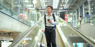 一名年轻人拿着行李箱站在人行道上，一边使用智能手机。