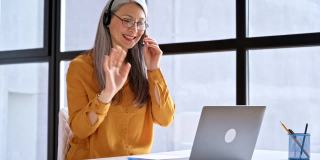 亚洲中年美女用笔记本电脑进行虚拟在线会议，白发苍苍的商务女士在网上进行视频会议交流，坐在现代的办公室里，进行在线交流的概念