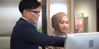 经理正在培训穆斯林员工。经理和员工讨论电脑工作。