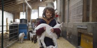 小男孩抱着小山羊站在牲口棚里