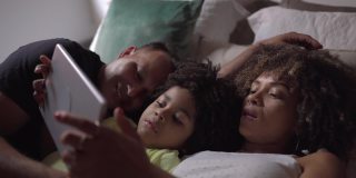 家人躺在床上用平板电脑看视频或电影