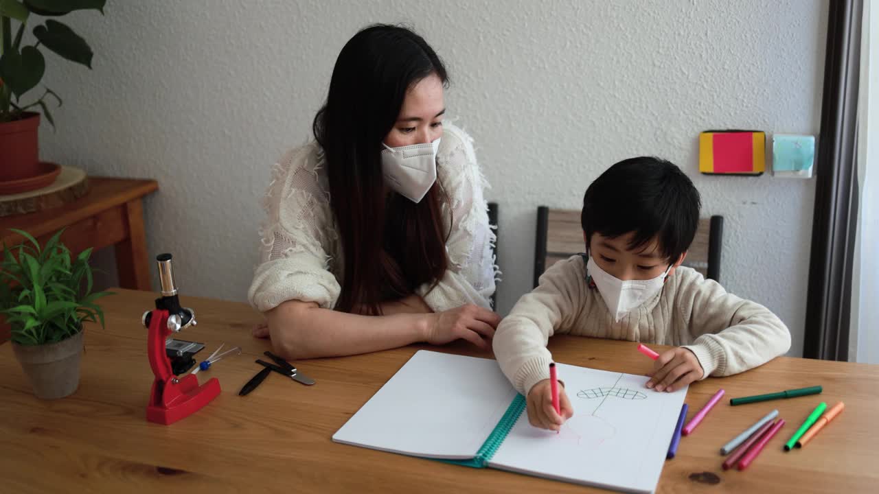 亚洲教师或母亲带着口罩与孩子一起画画