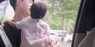亚洲年轻的成年父亲把玩他的宝贝女儿放在车内的驾驶座上，宝宝玩方向盘假装开车在家庭旅行中，家庭成员幸福的纽带