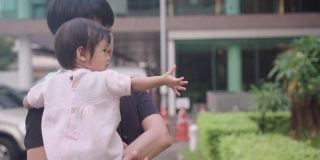 亚洲父亲抱着婴儿环视四周的树木花园公园、停车场，照顾孩子学习和发展，养育亲情，孩子的天真无邪，孩子的好奇心，家庭团聚