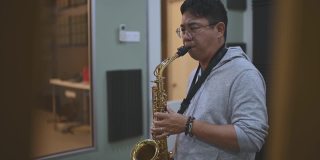 亚洲华人中年男子学习乐器演奏萨克斯在音乐工作室班