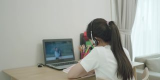 一名亚洲少女在学校因新冠肺炎疫情关闭期间，在家中的客厅通过笔记本电脑与老师在线学习数学。