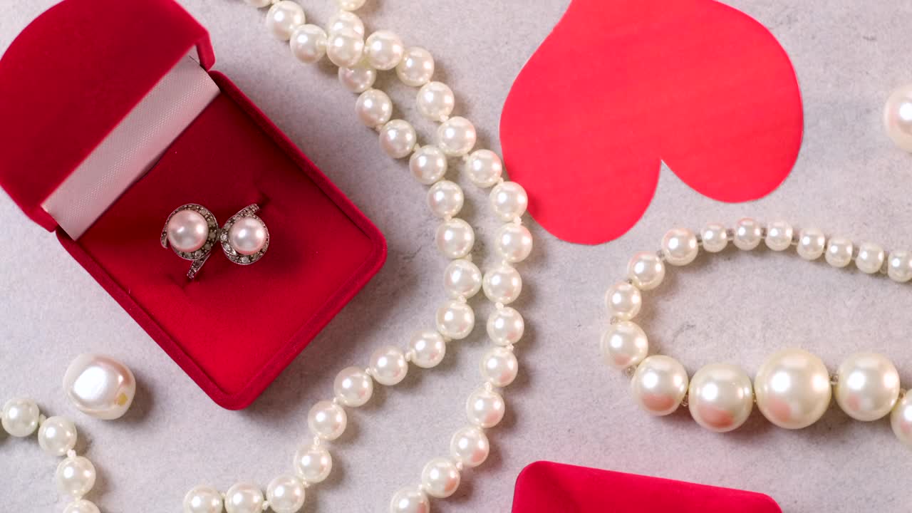 红盒子里的金戒指和珍珠。情人节的浪漫背景有宝石、礼物、订婚戒指等。求婚、婚礼或节日礼物的概念。贺卡旋转