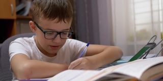 戴眼镜微笑的小男生用笔记本用笔写字，用智能手机说话