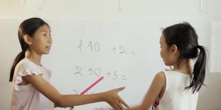 快乐的亚洲女孩用白板教姐姐数学，女孩在家里做运动，COVID-19期间在家自学。