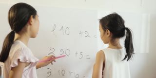 快乐的亚洲女孩用白板教姐姐数学，女孩在家里做运动，COVID-19期间在家自学。