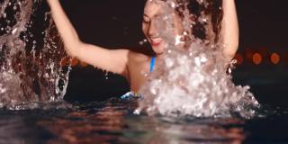 年轻迷人的女性潜水在一个温泉健康中心游泳池的水。用红色摄像机拍摄，4K格式。那个长着漂亮眼睛的女孩晚上在游泳池里看着镜头。