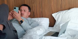 一个男人躺在酒店房间的床上给手机充电