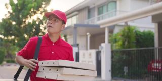 穿着红色制服的亚洲送货员搬运食物和披萨，晚上走着找客户的地址。邮差和快递杂货配送服务理念。