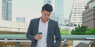 聪明的亚洲年轻商人在城市里使用智能手机。拿着电话的男人微笑着走到外面的办公室。以电信和移动网络为经营理念。