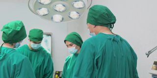 医院手术室的一组医生。多元化的团队，亚洲专业的外科医生和护士缝合手术成功后感到高兴和鼓掌。男人微笑着，摘下面具