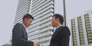 背景中，亚洲商人在城市建筑中握手。合作协议谈判完成后即成功。商业交易，合并和收购概念。