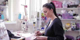 年轻女裁缝坐在缝纫机上缝东西的肖像。女裁缝为服装生产持有纺织品。