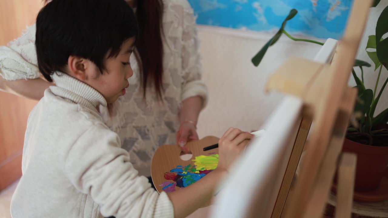 亚洲母亲和儿子有乐趣的绘画活动在画布上在家