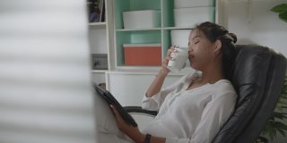 亚洲妇女她在家里工作她在工作的时候喝咖啡。