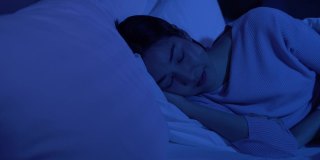 安静漂亮的年轻女人晚上闭着眼睛睡在她舒适的床上，盖着毯子。