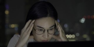 一个戴着眼镜，有思想的年轻女商人工作到深夜，因为不能看笔记本电脑而感到压力。