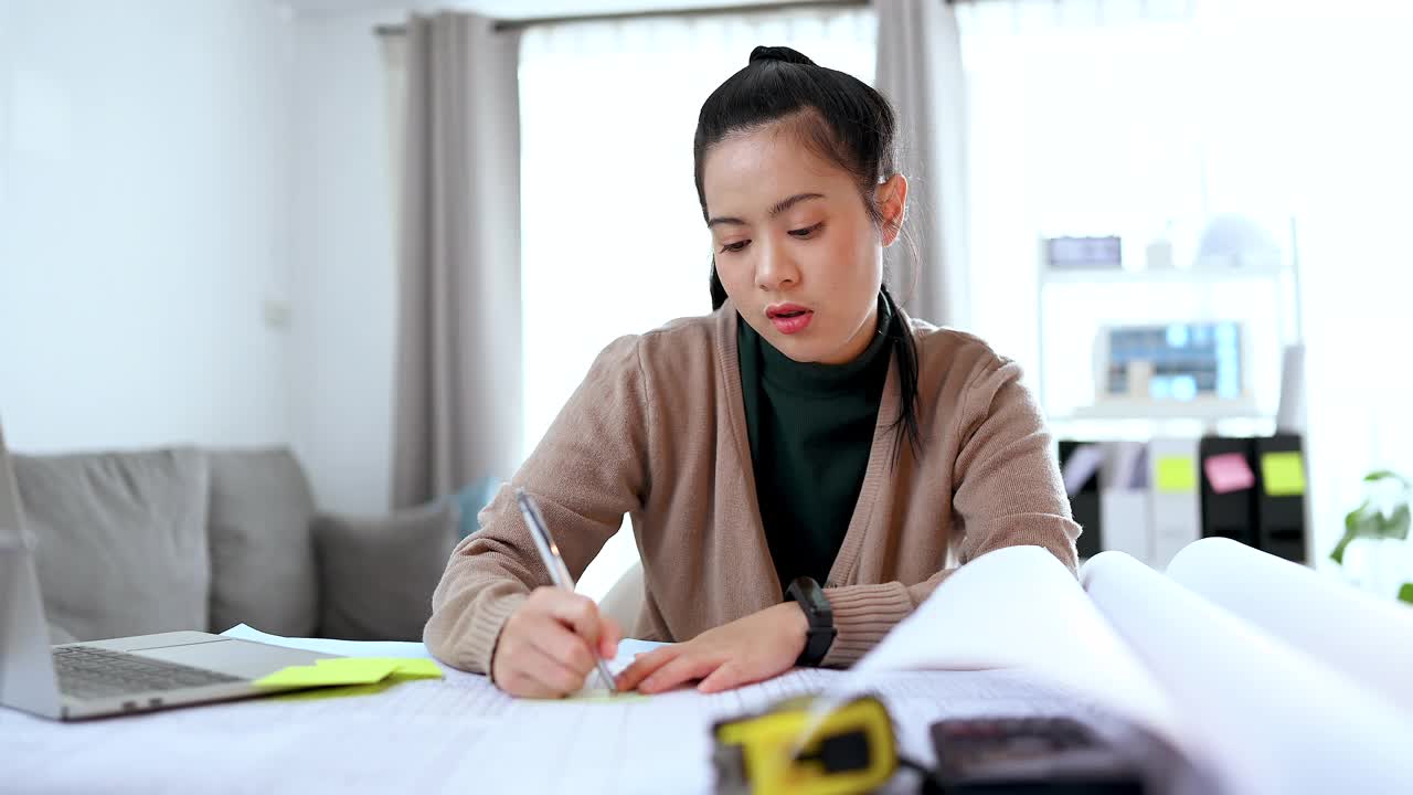 亚洲女建筑师在家庭办公室的便利贴上写字。居家办公建筑师和工程师的概念。