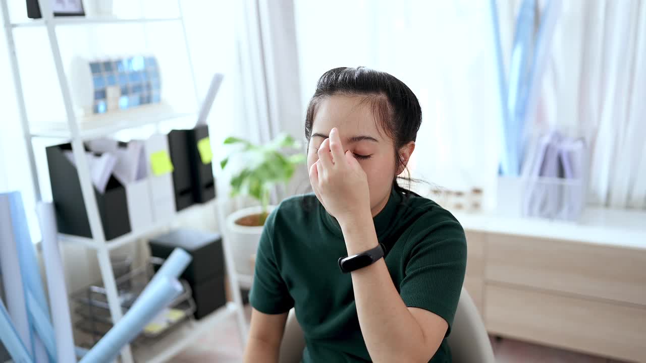 亚洲女建筑师下班后感到压力和头痛，在家工作，她很累，坐下来休息她的眼睛。建筑师和工程师的概念。