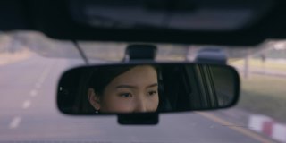 近距离亚洲妇女驾驶汽车反映在后视镜上的道路