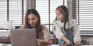 亚洲女儿给母亲肩部按摩工作时使用笔记本电脑数字技术在家，幸福家庭一起工作的理念。