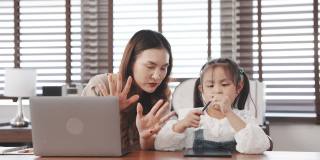 亚洲母亲教女儿做家庭作业计算数字数学后，从学校回家，母亲使用笔记本电脑数字技术工作。