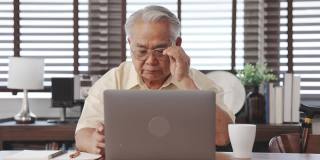 快乐的老年男性使用笔记本电脑搜索健康保险网上网站上的笔记本电脑购买保险的退休坐在家里，老年人健康的生活方式的概念。