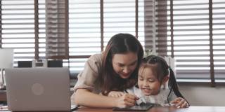 亚洲母亲教女儿做家庭作业后，从学校在家里，母亲工作使用笔记本电脑数字技术。