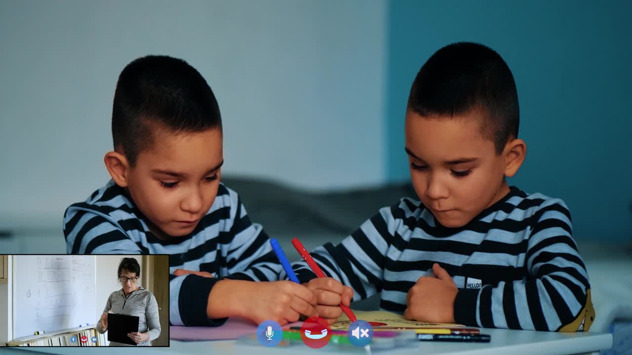 两个双胞胎小男孩在远处的学校教书，一个女老师通过视频电话教学。在屏幕上，年轻的学生在学校上课，老师在家里授课