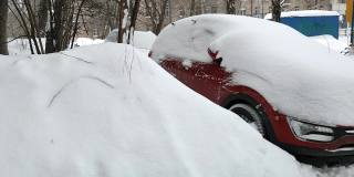 一辆覆盖着厚厚的积雪的红色轿车停在一所积着厚厚的积雪的房子的院子里