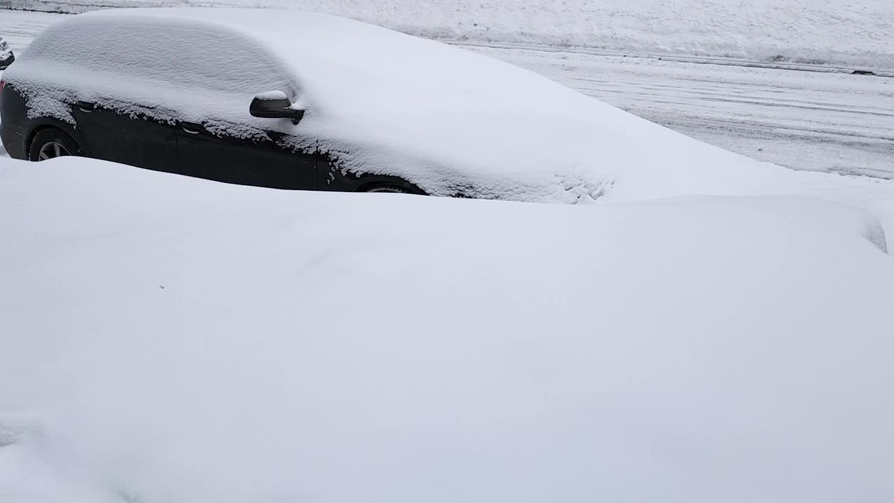 一辆被雪覆盖的黑色轿车停在一个巨大的雪堆后面的路上