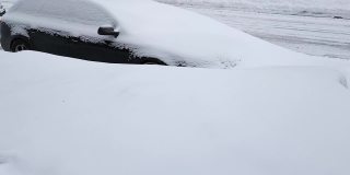 一辆被雪覆盖的黑色轿车停在一个巨大的雪堆后面的路上