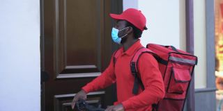 一名非洲男子戴着医用口罩骑自行车送餐，以应对冠状病毒疫情——带安全措施的送餐职业