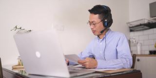 亚洲华人中年男子正在厨房里上网络课，早上还在用笔记本电脑