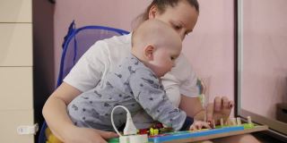 年轻的母亲和她的男婴在家里的地板上玩着忙板。益智玩具。Busy-board对孩子们。木质棋盘游戏。中景镜头。