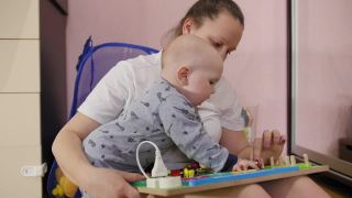 年轻的母亲和她的男婴在家里的地板上玩着忙板。益智玩具。Busy-board对孩子们。木质棋盘游戏。中景镜头。视频素材模板下载