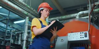 一位年轻的女工程师站在生产车间，记录技术设备的读数。底部视图。现代工业和制造业