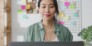 亚洲商业女性使用笔记本电脑与同事在视频通话中讨论计划，而智能工作在家客厅。