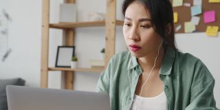 亚洲商业女性使用笔记本电脑与同事在视频通话中讨论计划，而智能工作在家客厅。