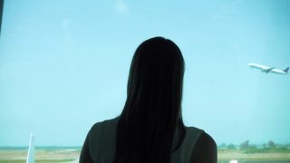 一名女子站在机场候机楼望着窗外的飞机起飞，在蓝天中飞翔视频素材模板下载