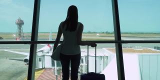 一个女人带着行李箱站在机场候机楼看窗外的剪影