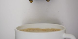 咖啡滴进满杯的白色杯子里，泡沫是棕色的
