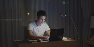 在家里工作的亚洲男人会在深夜坐在电脑前，看起来很紧张。