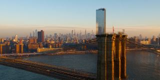 布鲁克林大桥鸟瞰图与遥远的曼哈顿地平线横跨东河和日出。无人机视频与全景轨道和上升的摄像机运动。
