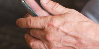 老年人学习使用电子产品的主题。特写一位老人的皱纹的手拿着智能手机，试图打开一个互联网页面。选择性聚焦，浅景深