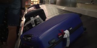在机场大楼里，人们拿着行李在传送带前排队